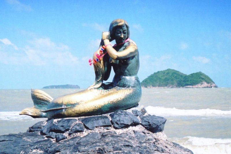 รูปปั้นนางเงือกนั่งหวีผมบนโขดหินริมหาดสมิหลา มีเกาะกลางทะเลเป็นฉากหลัง